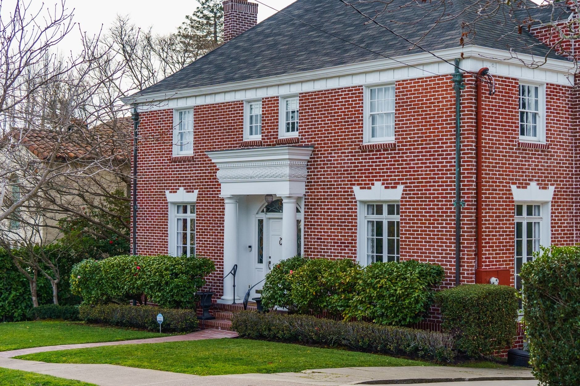 Elegant traditional red brick home with lush garden, showcasing classic American architecture.